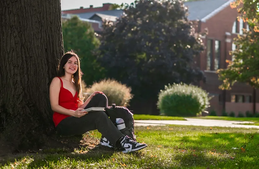 Katie Greer sits under a tree and smiles at the camera.