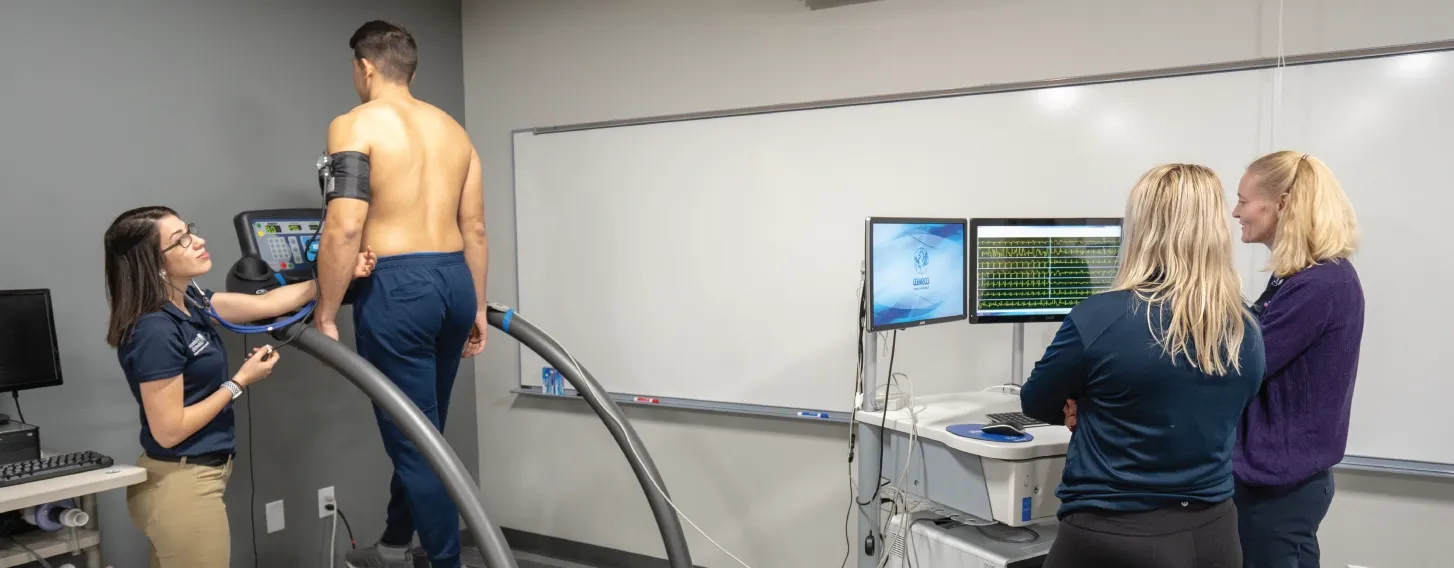 A man exercising on a treadmill while three women monitor his responses.