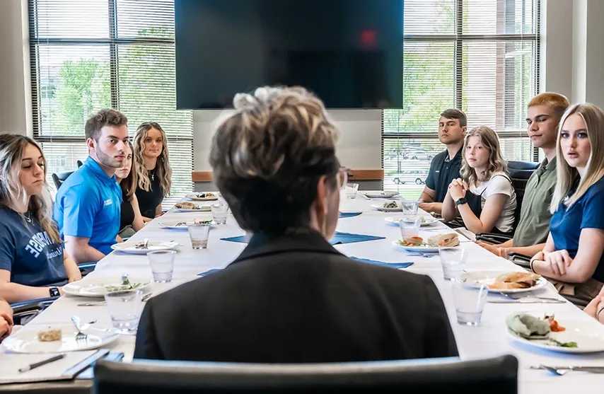 Amy Novak sits a table with student leaders. The plates on the table are filled with various amounts of food.